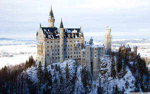 Castelo nevado em uma colina cercado por árvores perenes e um vale congelado. — Castelo Papéis de Parede