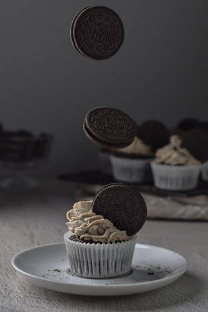Cupcake de chocolate con galletas Oreo flotando sobre él en un plato blanco. — Cupcake Fondos de pantalla