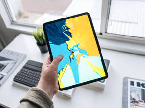Hånd, der holder tablet med farverigt abstrakt tapet på hvidt skrivebord nær vindue — iPad Mini Wallpapers