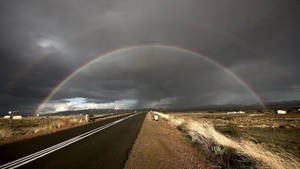 Arcoíris doble sobre una carretera del desierto bajo nubes de tormenta. — Arcoíris Fondos de pantalla