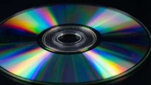 Un CD brillante que refleja colores de arcoíris sobre una superficie negra.