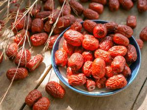 Een kom met rode jujubes op een houten tafel met gedroogde takken. — Data Achtergronden
