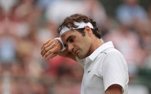 Roger Federer che si asciuga il sudore durante una partita di tennis con spettatori sullo sfondo. — Federer Sfondi