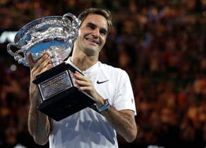 Roger Federer sorride mentre tiene un grande trofeo di tennis argentato di notte. — Federer Sfondi