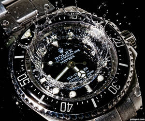 Nærbillede af et Rolex Sea-Dweller ur med vand, der sprøjter omkring dets ansigt. — Ur Wallpapers