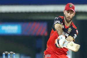 Cricket player swinging bat during night match under stadium lights. — Challengers Wallpaper