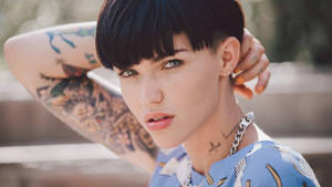 A tattooed woman with short black hair looks at the camera outdoors. — Ruby Rose Wallpaper