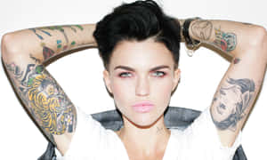 A tattooed woman with short dark hair and intense gaze poses with arms raised. — Ruby Rose Wallpaper