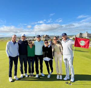 Syv golfspillere poserer på et grønt område med et rødt flag og blå himmel bag dem. — Golfbane Wallpapers