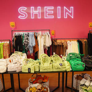 Interior de tienda minorista con paredes rosas letrero neón y estantes de ropa y bolsos. — She Fondos de pantalla