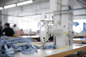 Máquina de coser industrial blanca cosiendo tela azul en una fábrica textil. — She Fondos de pantalla