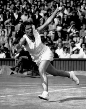 Female tennis player serving during a match on grass court with spectators. — Legend Wallpaper