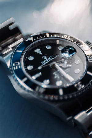 Et luksuriøst Rolex Submariner-ur med sort skive og stålarmbånd på blå overflade. — Sølv Wallpapers