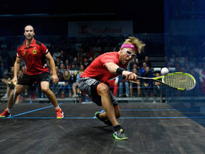 Two male squash players in red uniforms competing intensely on a glass-walled court. — Gym Wallpaper