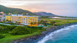 Luxury hotel on black sand beach at sunset with turquoise ocean and green hills — Hotel Wallpaper