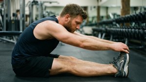 Man stretching leg on gym floor surrounded by weights taustakuva