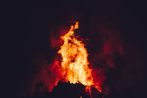 Un grande fuoco che brucia intensamente di notte con fiamme arancioni brillanti e fumo rosso. — Fuoco Sfondi