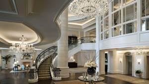 Grand mansion foyer with curved staircase chandeliers and marble columns. — Hotel Wallpaper