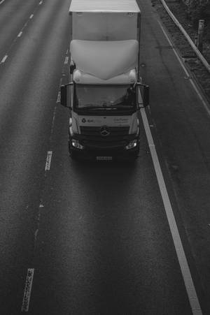 En stor hvid lastbil kører ned ad en våd motorvej ved skumringstid i sort-hvid. — Lastbil Wallpapers