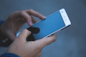 Hender som holder en hvit smarttelefon med en blå skjerm. — Mobile Bakgrunner