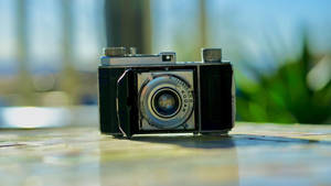 Vintage Kodak-camera op houten oppervlak met groene achtergrond en zonlicht. — Camera Achtergronden