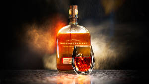 Woodford Reserve bourbonflaske og glass med is på en bar med røyk og varm belysning.