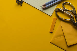 Materiais de escritório como tesouras, lápis e um envelope em um fundo amarelo. — Amarelo Papéis de Parede