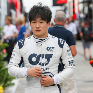 Young Asian race car driver in AlphaTauri suit adjusting zipper at race track. — Blue Wallpaper
