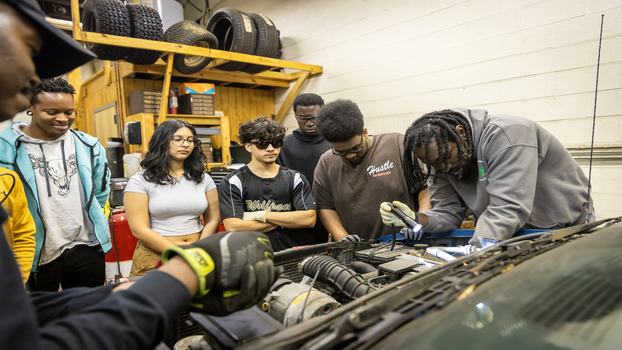 Students with staff learning how to work on automotive repair on a truck engine