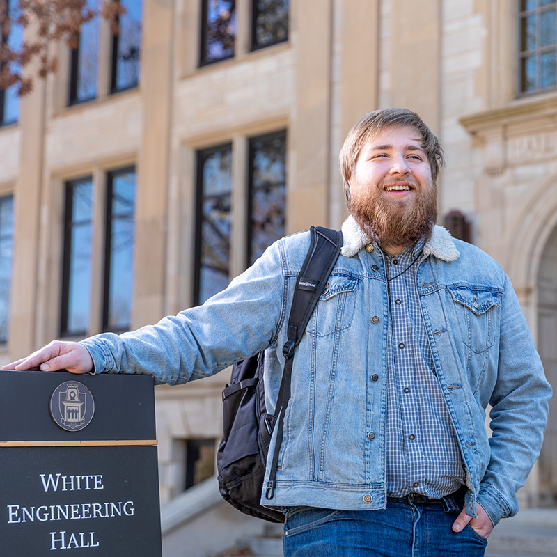Jonah in a denim jacket with a backpack outside White Engineering Hall on campus.